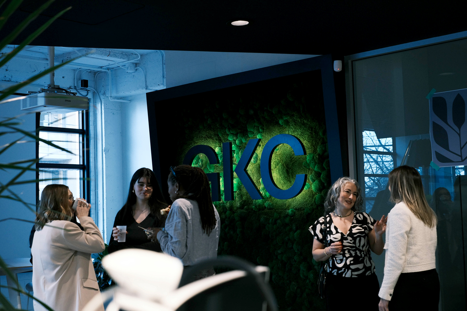People having a talk and a drink in front of the green wall with GKC's logo in their Montreal offices.