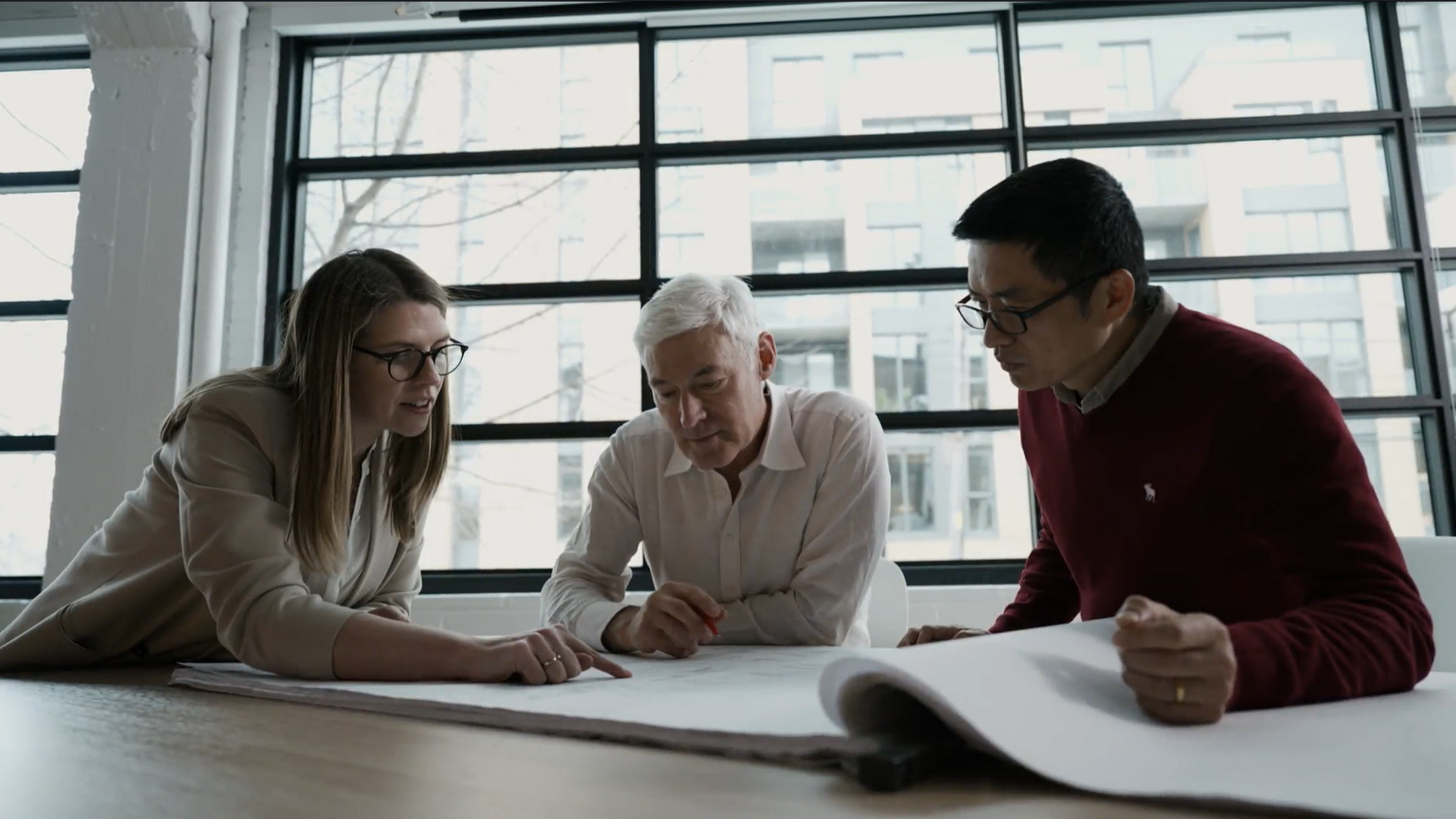 Trois membres de l’équipe analysent un plan d’architecture au bureau chef de GKC Architecture et Design.